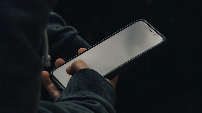 Jemand hält ein Smartphone vor dunklem Hintergrund.