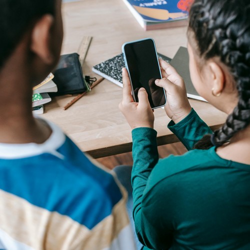Kinder an einem Schultisch halten ein Smartphone