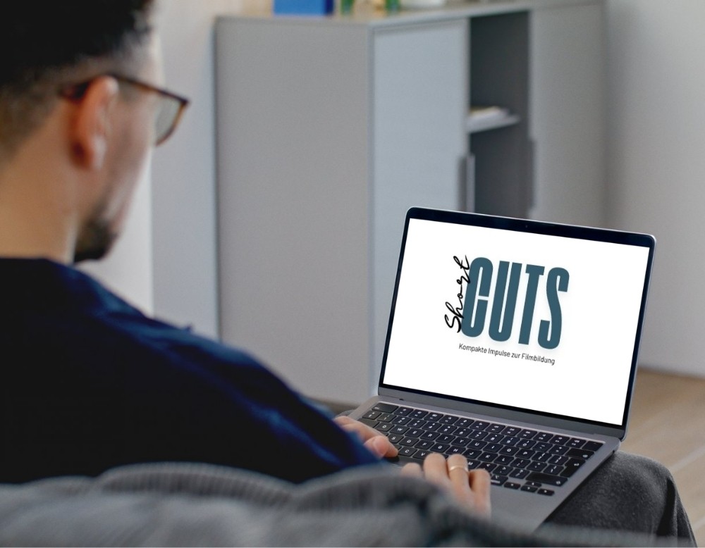 Eine Person sitzt am Laptop, auf dem Bildschirm ist das Logo von ShortCUTS zu sehen.