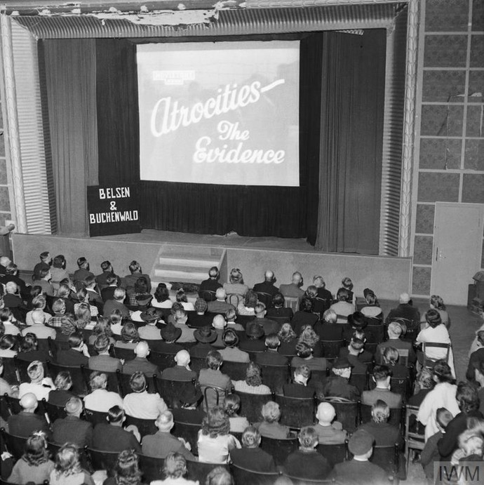 Schwarzweißfoto: Aufnahme eines Kinosaals mit Leinwand und Zuschauern: Die Leinwand zeigt den Filmtitel: „Atrocities – The Evidence“