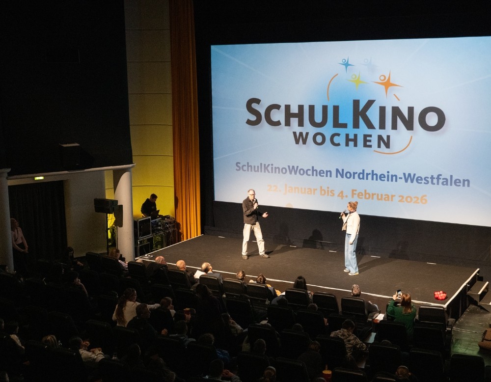 Zwei Moderatoren vor dem Logo der SchulKinoWochen NRW
