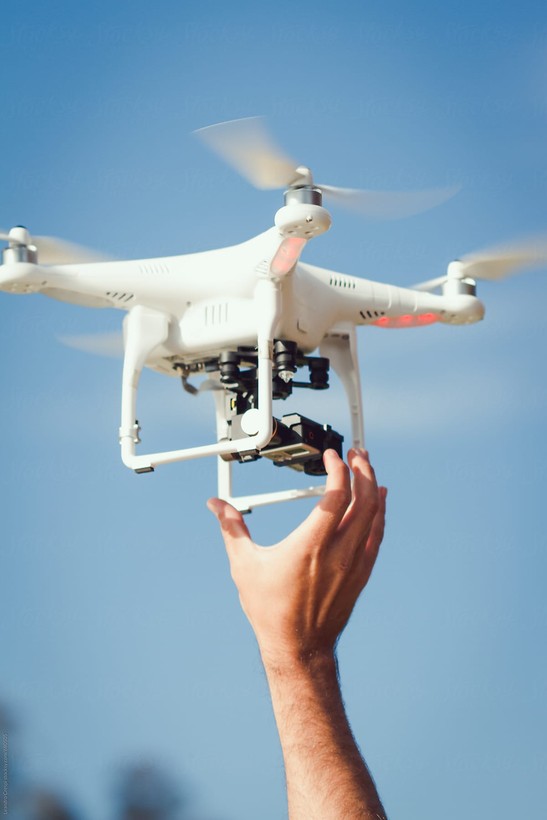 Eine weiße Drohne wird von einer Hand in die Höhe gehoben.