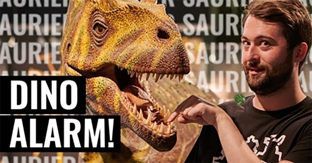 Ein junger Mann hält seine Hand in das geöffnete Maul eines Dinosauriers
