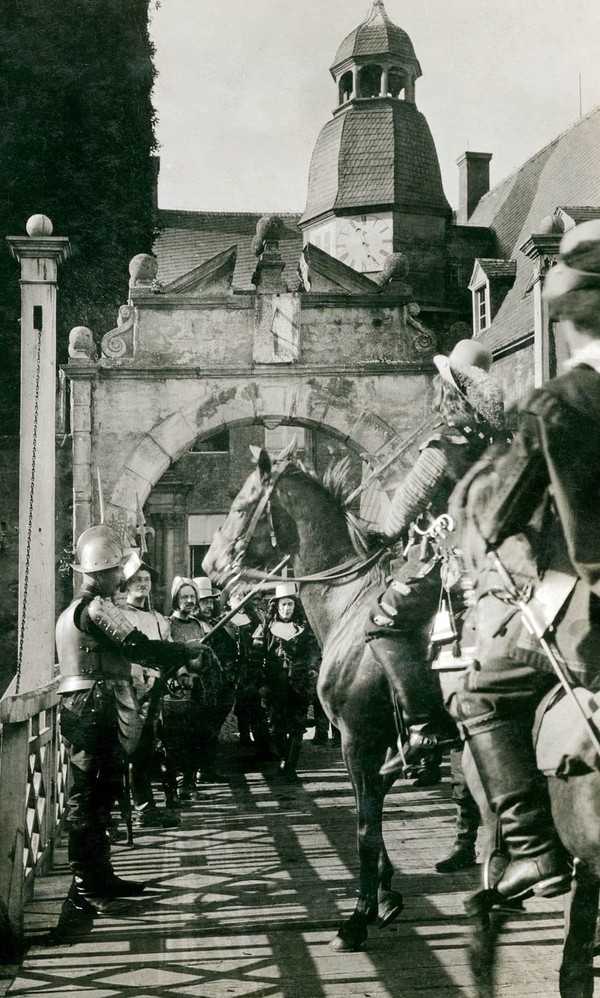 Soldaten auf Pferden stehen vor den Toren einer Burg.