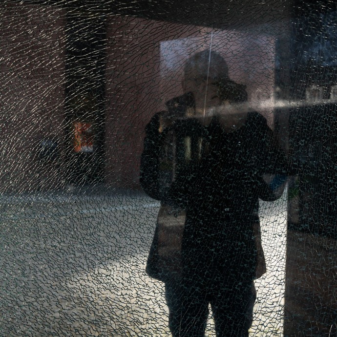 Spiegelung des Fotografens Veit Mette, während er vor der Kunsthalle Bielefeld durch gesprungenes Glas hindurchfotografiert (vergrößerte Bildansicht wird geöffnet)