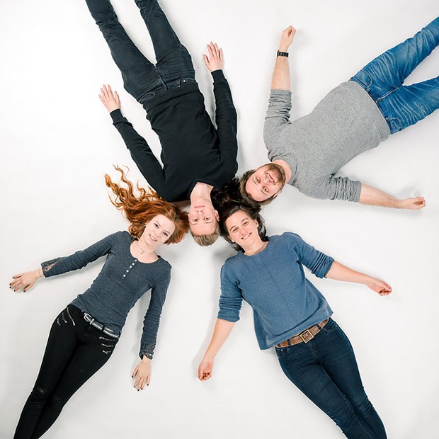 Vier Jugendliche liegen sternförmig angeodnet auf einem weisse Untergrund.
