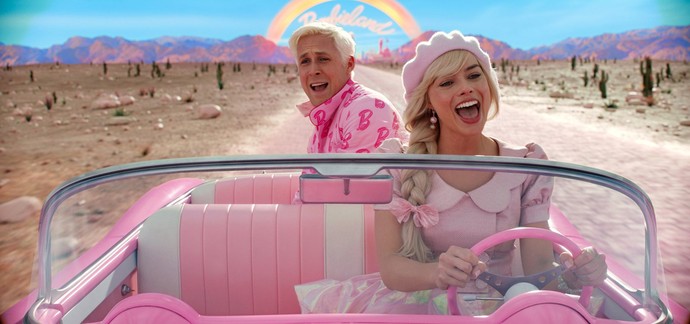 Filmstill aus "Barbie". Barbie und Ken in Frontalansicht in rosa Cabrio.