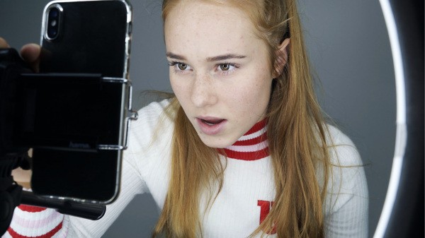 Eine junge Frau bedient ein Smartphone, das in einem Ringlicht montiert ist. Eine junge Frau bedient ein Smartphone, das in einem Ringlicht montiert ist.