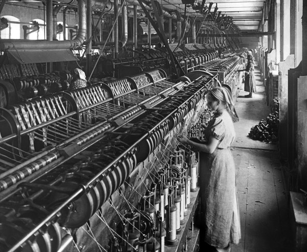 Eine junge Frau im Kleid und mit Kopftuch steht um 1910 vor einer Vorspinnmaschine der Ravensberger Spinnerei in Bielefeld.